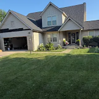 Before: the same two-story home with its original tan siding, partly stripped above the garage